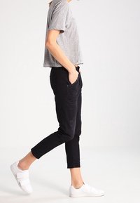 Graues, kurzes T-Shirt, schwarze, eng geschnittene Jeans mit fransigem Saum und weiße Slip-On-Schuhe. Einfaches Design mit relaxed Fit und minimalen Details.