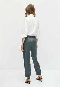 Chemise blanche à boutons, manches retroussées, associée à un pantalon gris avec une taille élastique et des poignets fuselés. Texture de tissu lisse.