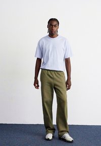 T-shirt de manga curta lilás claro combinado com calças relaxadas de tom verde-azeitona. Ténis brancos completam o conjunto. Design simples e casual.