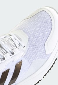 Białe buty sportowe z fakturowanym cholewką w połączeniu jasnego i ciemnego odcienia bieli, z brązowymi metalicznymi akcentami i sznurowanym zapięciem.