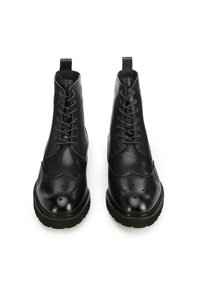 Botines de cuero negro con cordones, con detalles de brogue, punta redonda y suela gruesa y texturizada. Cuenta con una lengüeta en la parte superior.