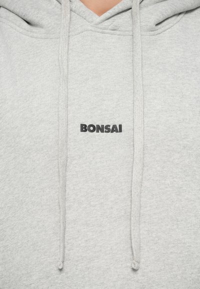 Heledad hallhall, millel on ees kangaroo tasku, nöörid ja sõna "BONSAI" julgete mustade tähtedega.