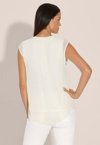 Korte mouwen, crèmewit blouse met een soepele textuur, ronde zoom en een licht transparante achterkant. Eenvoudig, minimalistisch ontwerp.