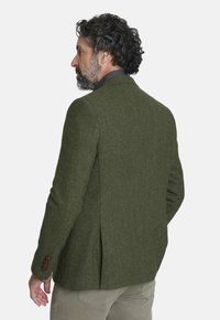 Blazer de lana verde oliva con una tela texturizada, corte entallado, abertura en la parte posterior y acentos de botones burdeos en las mangas.