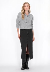 Cardigan gri tricotat cu detaliu sub formă de fundiță, fustă din denim negru cu deschidere frontală și cizme din piele neagră până la genunchi. Design simplu, potrivire confortabilă.