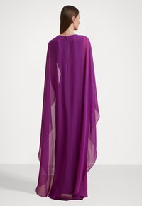 Purppuran chiffon-kapa, jossa on virtaava muotoilu, avoimet sivut ja pieni takakiinnitys. Kevyt kangas korostaa laskeutuvuutta.