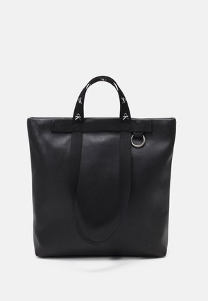 Borsa a mano in pelle nera con due manici in tessuto, un anello decorativo e una texture liscia. Presenta un design minimalista e un dettaglio con logo in rilievo.