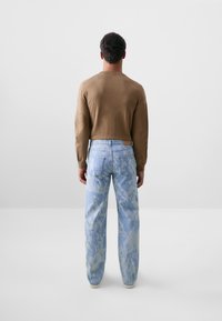 Camisa de manga larga marrón combinada con unos vaqueros de mezclilla azul claro con un patrón de camuflaje. Los vaqueros tienen un corte relajado y bolsillos traseros.