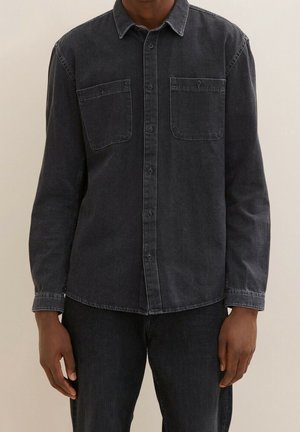 Homme portant une chemise en denim noire à manches longues avec deux poches poitrine et un pantalon en denim noir assorti.