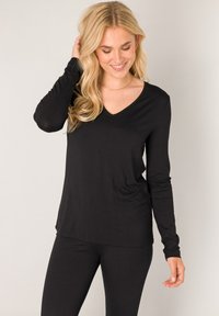 Black long-sleeve top with a V-neck design, made from soft fabric. The fit is relaxed, paired with matching black leggings.