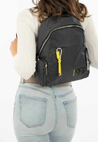 Svart texturerad ryggsäck med blixtlås, en gul accentdetalj och företagslogotyp. Har justerbara remmar och en rymlig huvudfack.