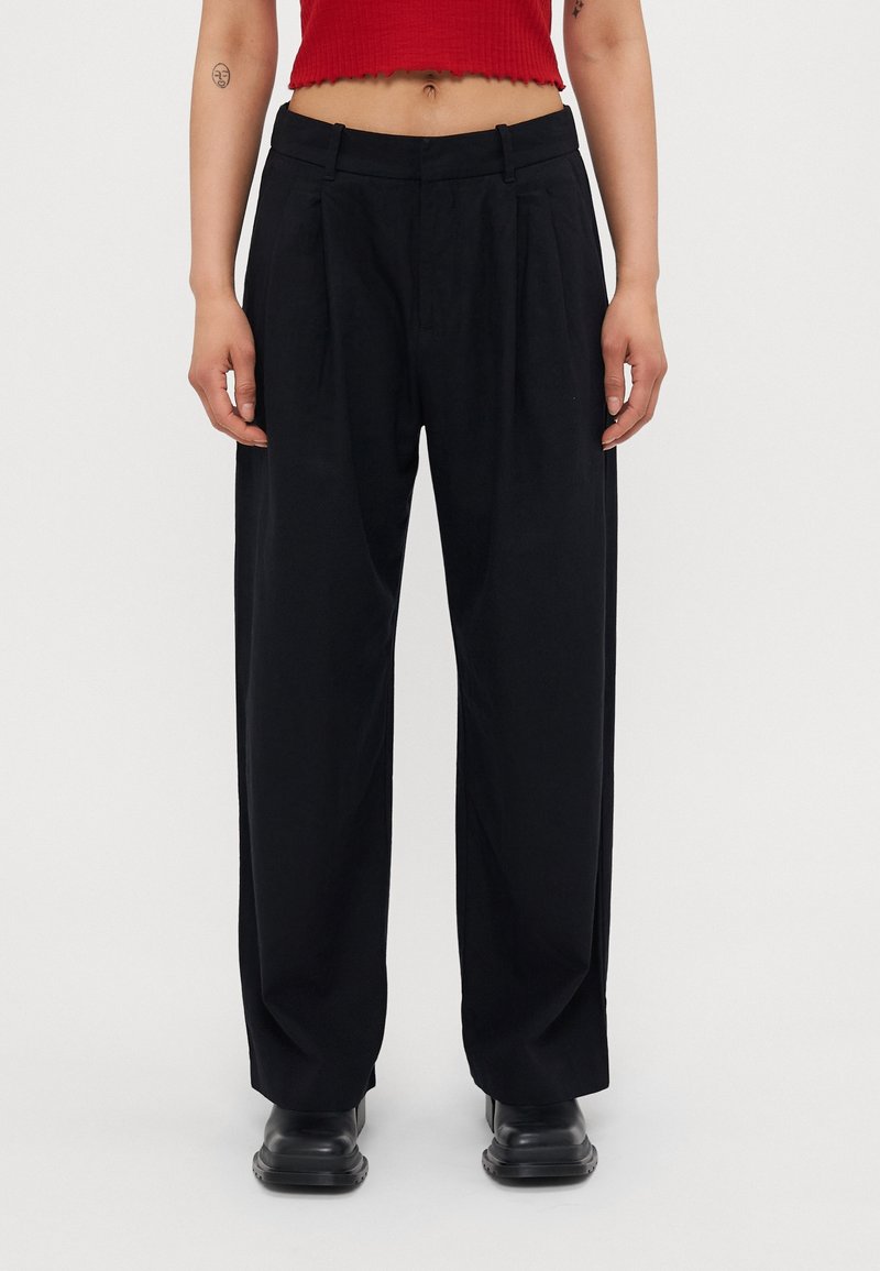 Czarne plisowane spodnie z wysokim stanem, szeroką nogawką i gładkiego materiału, zestawione z czarnymi botkami za kostkę.