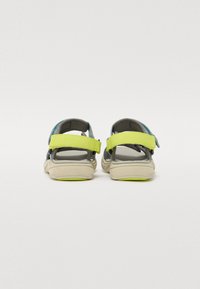 Bakside av sandaler med en lys grå såle, justerbare stropper i grønn og blå, og en teksturert fotinnlegg for komfort.