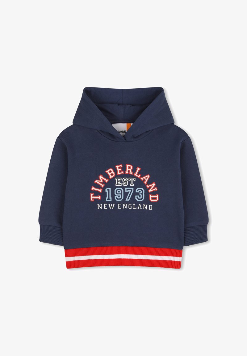 Sweat à capuche bleu marine avec ourlet rayé rouge et blanc. Présente un graphisme "TIMBERLAND EST 1973 NEW ENGLAND" en couleurs contrastantes.