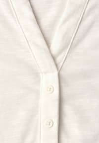 Cardigan blanc en tissu côtelé à col en V avec deux boutons blancs fermés au centre devant.