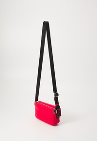 Red crossbody bag made of smooth material featuring a zip closure, adjustable black strap, and a compact rectangular shape.