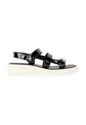 Sandale en cuir verni noir avec semelle plateforme blanche composée de trois brides, chacune avec un petit détail de logo blanc de la marque.