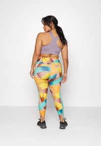 Sutiã desportivo roxo combinado com leggings de cintura alta com um padrão de folhas abstrato colorido em laranja, teal e castanho. Sapatos de atletismo pretos.