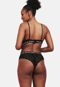 Set di bralette in pizzo nero e perizoma con spalline regolabili e cintura con logo. Presenta dettagli in pizzo floreale e una vestibilità elegante.
