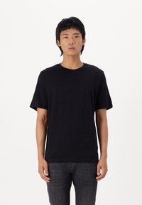 Zwarte katoenen T-shirt met korte mouwen en een ronde halslijn, gedragen met donkere jeans, met een eenvoudige, gladde textuur.