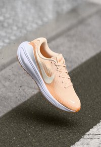 Helle Pfirsich-Laufschuhe mit einem atmungsaktiven Mesh-Obermaterial, weißer Mittelsohle und einem cremefarbenen Nike-Swoosh. Verfügt über minimale Schnürung und strukturierte Akzente.