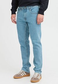 Vaqueros de mezclilla azul claro con corte recto, diseño de cinco bolsillos y costuras sutiles. Combinados con zapatillas grises con franjas blancas.