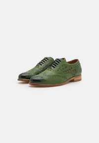 Scarpe in pelle verde con punta nera lucida, dettagli brogue e intricate motivi intagliati sui lati. Suola marrone, design con lacci.