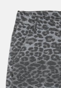 Sive traperice s crnim uzorkom leoparda. Uključuju prednji džep s vidljivim šavovima i detalj od metalne kopče.