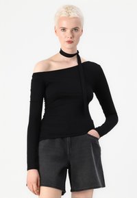 Zwarte off-shoulder top met lange mouwen, een aansluitend ontwerp, zachte textuur en een gestrikte halsdetail, gecombineerd met donkergrijze shorts.