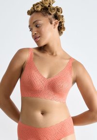 Bralette corail avec un décolleté en V et des bords festonnés, présentant un motif texturé. Matière douce et légère conçue pour le confort.