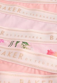 Ružičasta tkanina s cvjetnim uzorkom, prekrivena bijelom vrpcom sa natpisom "BAKER by TED BAKER" u zlatnom slovu, glatke teksture.