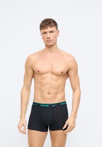 Czarne bokserki z teallogiem Nike na pasku. Materiał wydaje się gładki i dopasowany, z długością sięgającą do połowy uda.