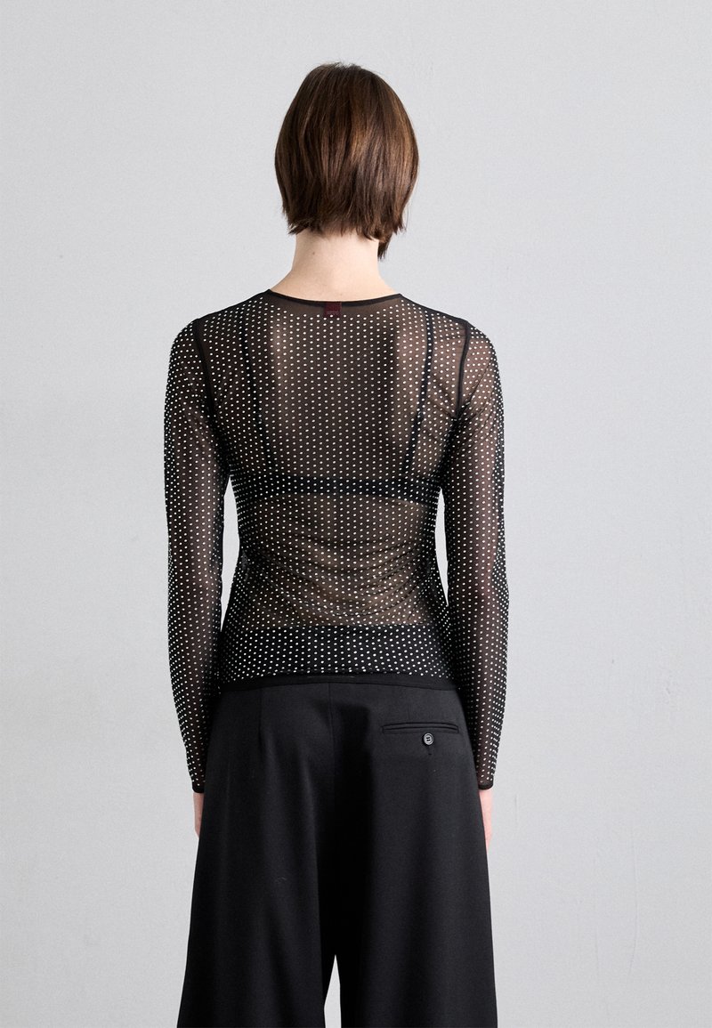 Top nero trasparente a maniche lunghe con pois bianchi, caratterizzato da un colletto rotondo e un design aderente. Indossato con pantaloni neri a vita alta.