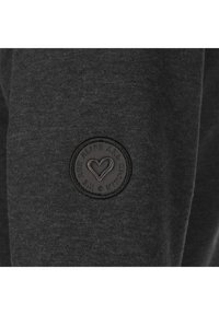 Tela de sudadera gris oscuro con un parche redondo y negro en relieve que presenta un diseño de corazón y el texto "WE ARE ALIFE AND KICKING."