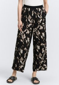 Pantalones de pierna ancha en un patrón abstracto en negro, crema y marrón; con pliegues en la parte delantera, cintura elástica y bolsillos laterales. Se llevan con sandalias planas.