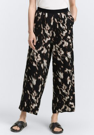 Pantalones de pierna ancha en un patrón abstracto en negro, crema y marrón; con pliegues en la parte delantera, cintura elástica y bolsillos laterales. Se llevan con sandalias planas.