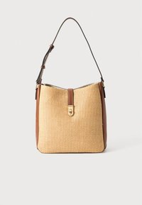 Tanflettet stråhåndtaske med brun læderbund, der har en guldlås og en justerbar skulderrem.