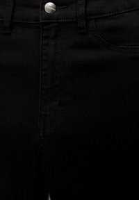 Détail d'un jean en denim noir montrant la fermeture par bouton, les passants de ceinture, la poche avant et les coutures.