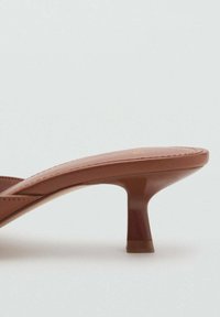 Brown heeled sandals with a glossy finish, featuring a thin strap and a unique, short stiletto heel. Smooth texture and minimalist design.