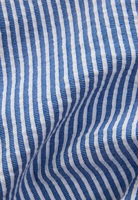 Tessuto di cotone con superficie testurizzata, caratterizzato da righe verticali alternate blu e bianche, che creano un effetto ondulato.