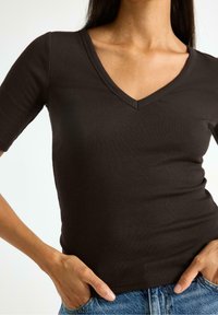 Top corto a maniche corte marrone con scollo a V, dalla vestibilità aderente, texture liscia e leggero stretch, abbinato a pantaloni di jeans blu.