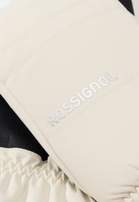 Primo piano di un guanto invernale beige con polsino elastico e logo "Rossignol" in lettere grigie sulla parte posteriore della mano.