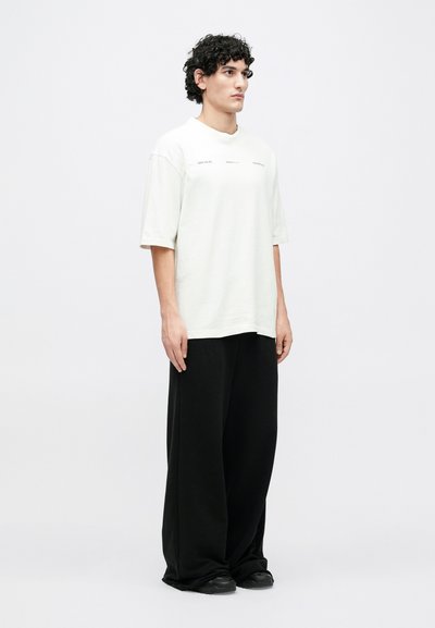 Voľné svetlosivé tričko s krátkymi rukávmi, s minimálnymi textovými prvkami. Kombinované so širokými čiernymi nohavicami a čiernou obuvou.