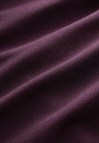 Texturerad tyg i djup lila, med en mjuk, slät yta och subtila veck och vågor som framhäver dess följsamma natur.