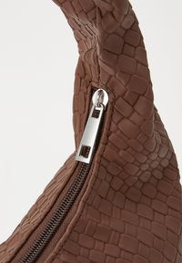Brun texturerad handväska med ett reptilmönster, utrustad med en silverfärgad dragkedja och dragremsor. Handtaget är böjt och mjukt att ta på.
