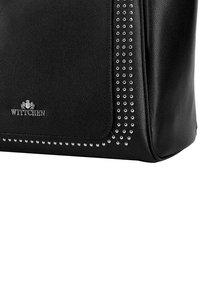 Svart läderhandväska med en slät textur, silvernitar längs en kant och en logotyp präglad på framsidan. Rektangulär design.