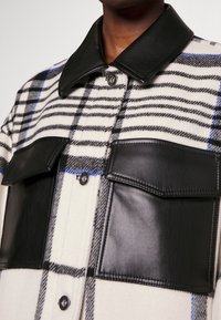 Checkered shirt jacket with a black leather collar and pockets, featuring a blend of white, black, and blue patterns, smooth texture.