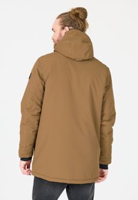 Brun vattentät parka med huva, med rak passform, sidofickor och en svart logotyp på vänster ärm. Slät textur, isolerad design.