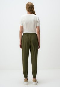 Olijfgroene joggerpants met elasten boorden, te combineren met een wit T-shirt. Zacht, ademend materiaal, casual ontwerp en comfortabele pasvorm.