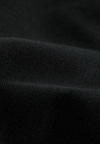 Tessuto nero con una superficie testurizzata, che mostra un primo piano del materiale tessuto. Il tessuto appare liscio e resistente, con una sottile profondità.